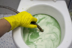 A hand in protective glove fixing clogged toilet, indoor closeup